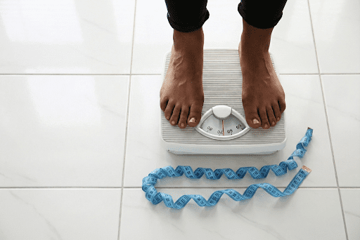 Person on a weighing scale with measuring tape symbolising weight loss progress